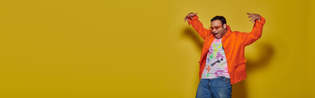indian man in sunglasses and vibrant attire looking down and gesturing on yellow background, banner