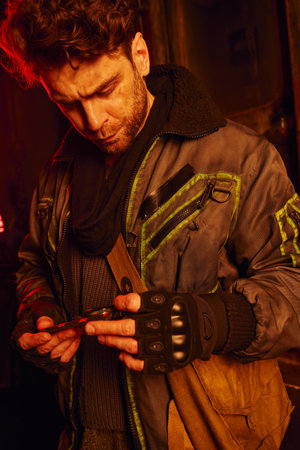 thoughtful man in worn clothes holding pressure gauge in subway carriage, post-disaster survival