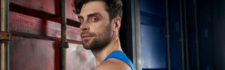 portrait of sportive unshaven man looking at camera near containers on street, bannerの写真素材