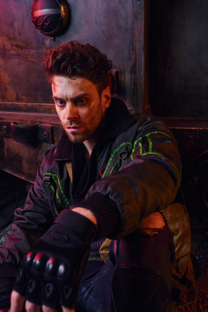 deep in thought man with unshaven scratched face sitting near rusty carriage in post-disaster subwayの写真素材