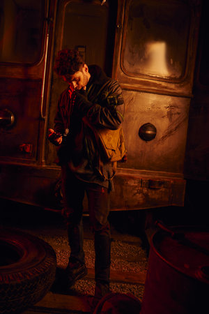 thoughtful man looking at spare part of rusty subway carriage in post-apocalyptic underground