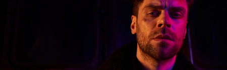 man with unshaven injured face looking at camera in red light of post-apocalyptic subway, banner