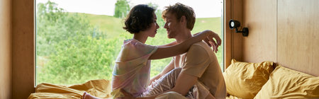 diverse couple looking at each other and sitting on bed in country house with forest view, banner