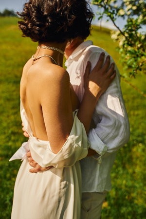 brunette bride in white dress standing with groom in green garden, newlyweds in countrysideの写真素材
