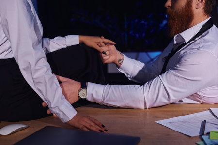 bearded tattooed businessman holding hand of african american woman sitting on desk, cropped viewの写真素材