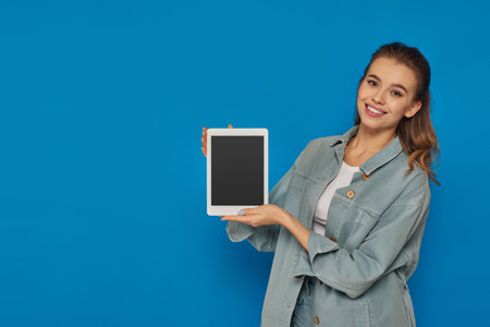 happy young woman holding digital tablet with blank screen on blue background, social mediaの写真素材