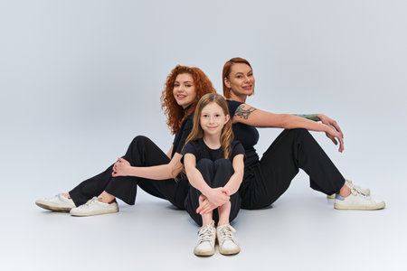 redhead family in matching clothes sitting together on grey backdrop, three female generationsの写真素材