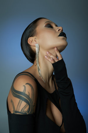 seductive woman with creepy makeup touching neck on blue and grey backdrop, halloween conceptの写真素材
