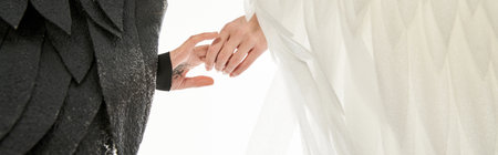cropped view of angel and demon with black and light wings holding hands on white, bannerの写真素材