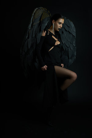 seductive woman in dark makeup and costume with demonic wings looking away on black, Halloweenの写真素材
