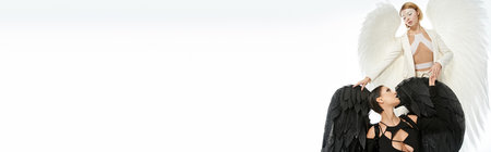 women in costumes of angel and demon looking at each other on white, spiritual warfare, bannerの写真素材