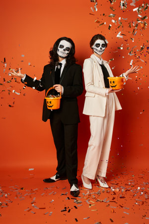 couple in skull makeup throwing shiny confetti from candy buckets on red, dia de los muertos partyの写真素材