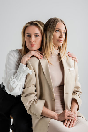 two elegant pretty sisters in business casual attire sitting on chairs and hugging, fashionの写真素材