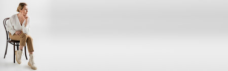 attractive woman in pastel outfit sitting on chair and looking away, style and fashion, bannerの写真素材