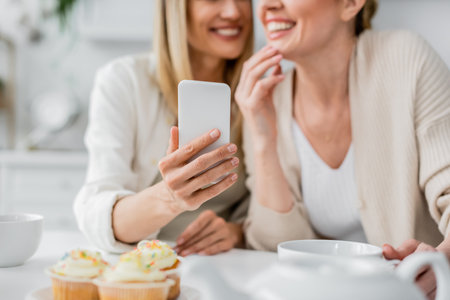 cropped view of two attractive sisters in cardigans making selfie on kitchen backdrop, bondingの写真素材
