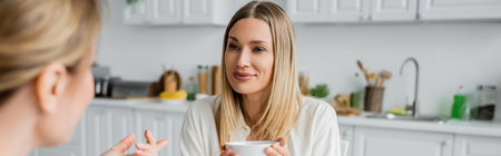 cropped view of two pretty lovely sisters talking and drinking tea, family bonding, bannerの写真素材
