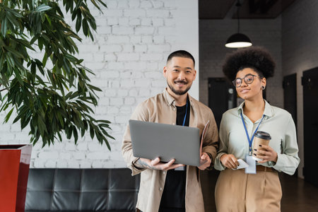 happy african american businesswoman and asian businessman with laptop, diverse office workers