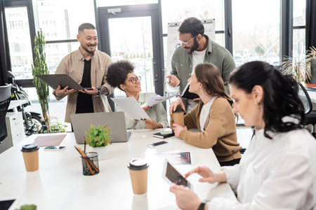 cheerful interracial business team discussing project and sharing ideas with team lead in coworkingの写真素材