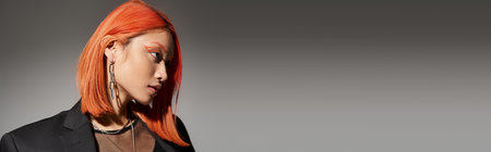 portrait of attractive asian woman with red hair and piercing looking away on grey backdrop, bannerの写真素材