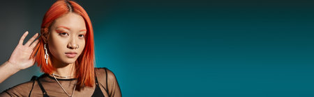 portrait of pierced asian woman with bold eye makeup and trendy earring on blue background, bannerの写真素材
