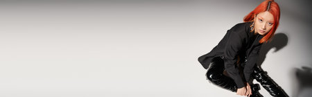 high angle of asian woman in sexy latex boots and blazer sitting on grey backdrop, bannerの写真素材