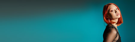 portrait of pierced asian woman with bold eye makeup looking at camera on blue background, bannerの写真素材