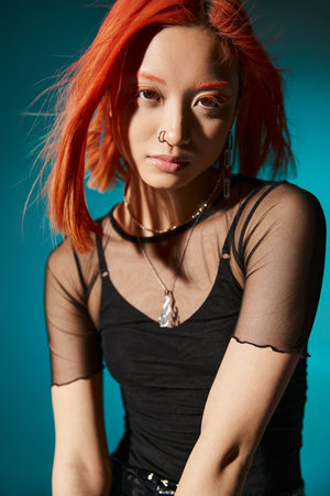 portrait of young asian woman with piercing posing in black transparent blouse on blue backdropの写真素材
