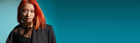 asian woman with red hair and nose piercing posing in oversized blazer on blue backdrop, bannerの写真素材