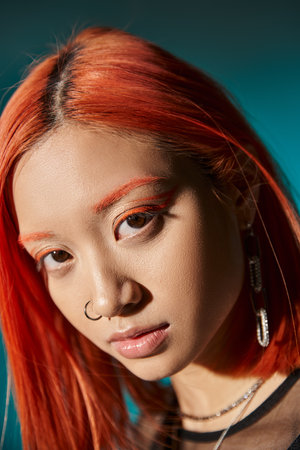 close up of mesmerizing asian woman with bold eye makeup looking away on blue background, youthfulの写真素材