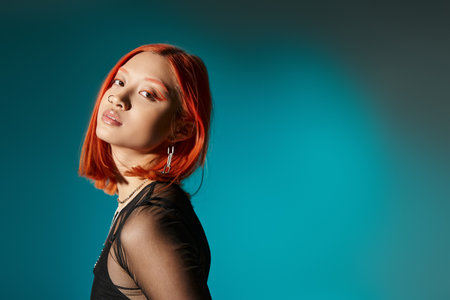 portrait of pierced asian woman with bold eye makeup looking at camera on blue backgroundの写真素材