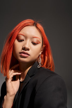 portrait of young asian woman with red hair, nose piercing and eye makeup posing on greyの写真素材