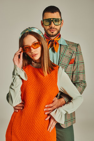man in plaid blazed embracing woman in orange dress and sunglasses on grey, retro-inspired fashionの写真素材