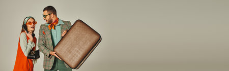 excited man with vintage suitcase near retro style woman talking on rotary phone on grey, bannerの写真素材