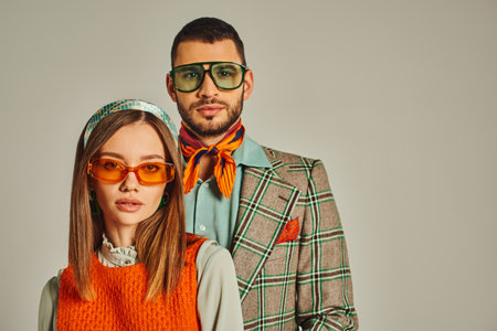young couple in elegant vintage clothes and sunglasses looking at camera on grey, fashion from pastの写真素材