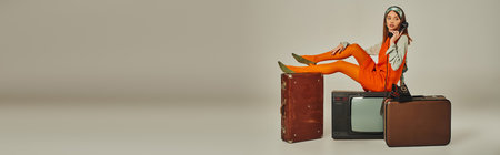 woman sitting on vintage suitcases and retro tv set while and talking on telephone on grey, bannerの写真素材