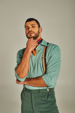 thoughtful man in suspenders and bright neckerchief looking at camera on grey, vintage fashionの写真素材