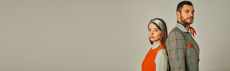 stylish couple in old-fashioned outfit standing back to back and looking at camera on grey, bannerの写真素材