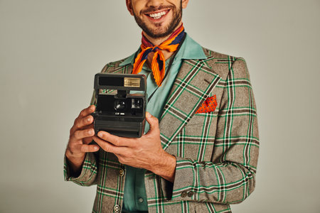 cropped view of smiling man in plaid jacket holding vintage camera on grey, retro-inspired lifestyleの写真素材