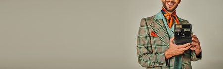 cropped view of happy man in checkered blazer taking photo on vintage camera on grey, bannerの写真素材
