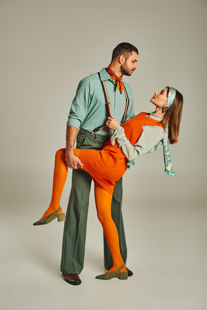 side view of stylish man in suspenders flirting with woman in bright clothes on grey, retro fashionの写真素材