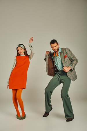 young couple in plaid jacket and orange dress dancing on grey, vintage fashion, full lengthの写真素材