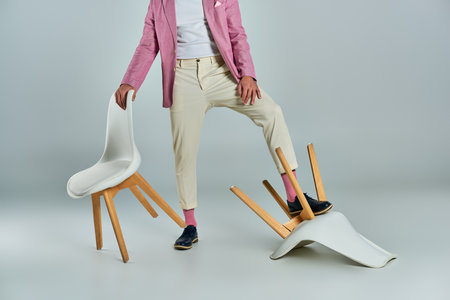 cropped view of man in lilac blazer and white pants posing with armchairs on grey, business fashionの写真素材