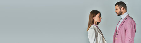 side view of young couple in stylish blazers looking at each other on grey, business fashion, bannerの写真素材