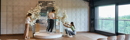 creative team arranging festive decor with white blooming flowers in modern event hall, banner
