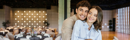 happy man hugging smiling girlfriend in decorated banquet hall, wedding preparation, bannerの写真素材