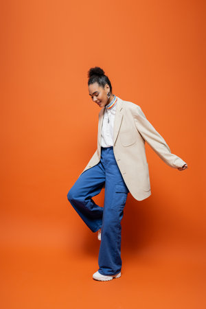 cheerful african american fashion model in beige blazer and blue pants smiling looking downの写真素材