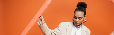 elegant young fashion model in stylish attire with bun and accessories holding orange frameworkの写真素材