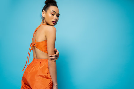 attractive african american woman in vibrant street clothing with hoop earrings looking at cameraの写真素材