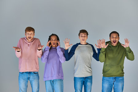 four shocked multicultural friends in colorful street attire on grey backdrop, cultural diversityの写真素材