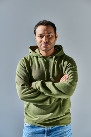 young indian man in khaki hoodie smiling with his hands crossed on chest on yellow backgroundの写真素材